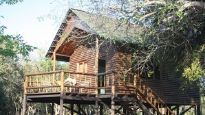 A wooden cabin with a balcony and stairs, surrounded by trees. - Bonamanzi Game Reserve (Hluhluwe)