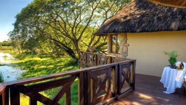 A thatched-roof structure with a wooden deck overlooking a river and lush greenery. - Bonamanzi Game Reserve (Hluhluwe)