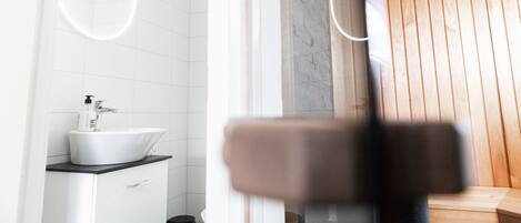 A modern bathroom with a white sink, a mirror with a circular light, and wooden paneling.
