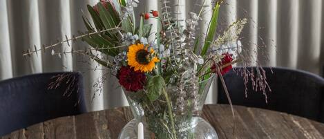 A table with a clear glass vase containing flowers and a candle, a magazine, and a hanging light fixture.