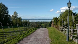 A gravel path leading to a lake with a wooden fence on one side and a lamp post on the other. - Villa Långbers (Tallberg)