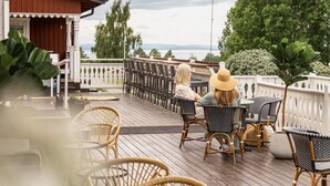 A wooden deck with wicker chairs and tables, overlooking a body of water. - Villa Långbers (Tallberg)