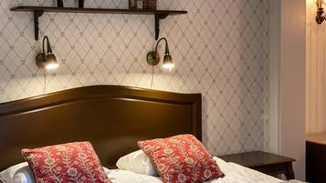 A neatly made bed with floral pillows, a wooden headboard, and a shelf above with decorative items and wall-mounted lights.