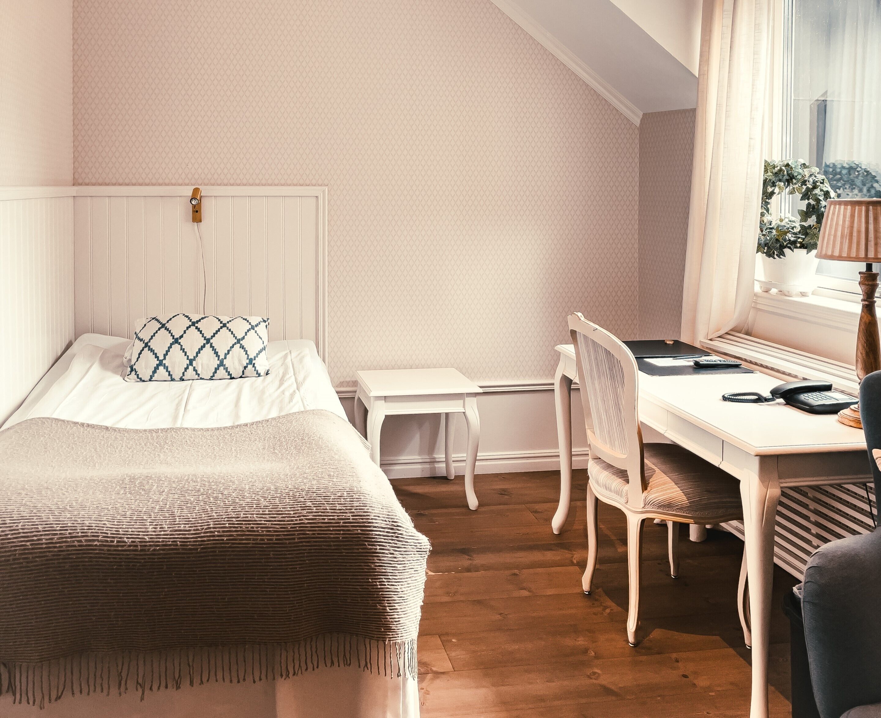 Un dormitorio con cama, escritorio, silla y ventana con cortinas.