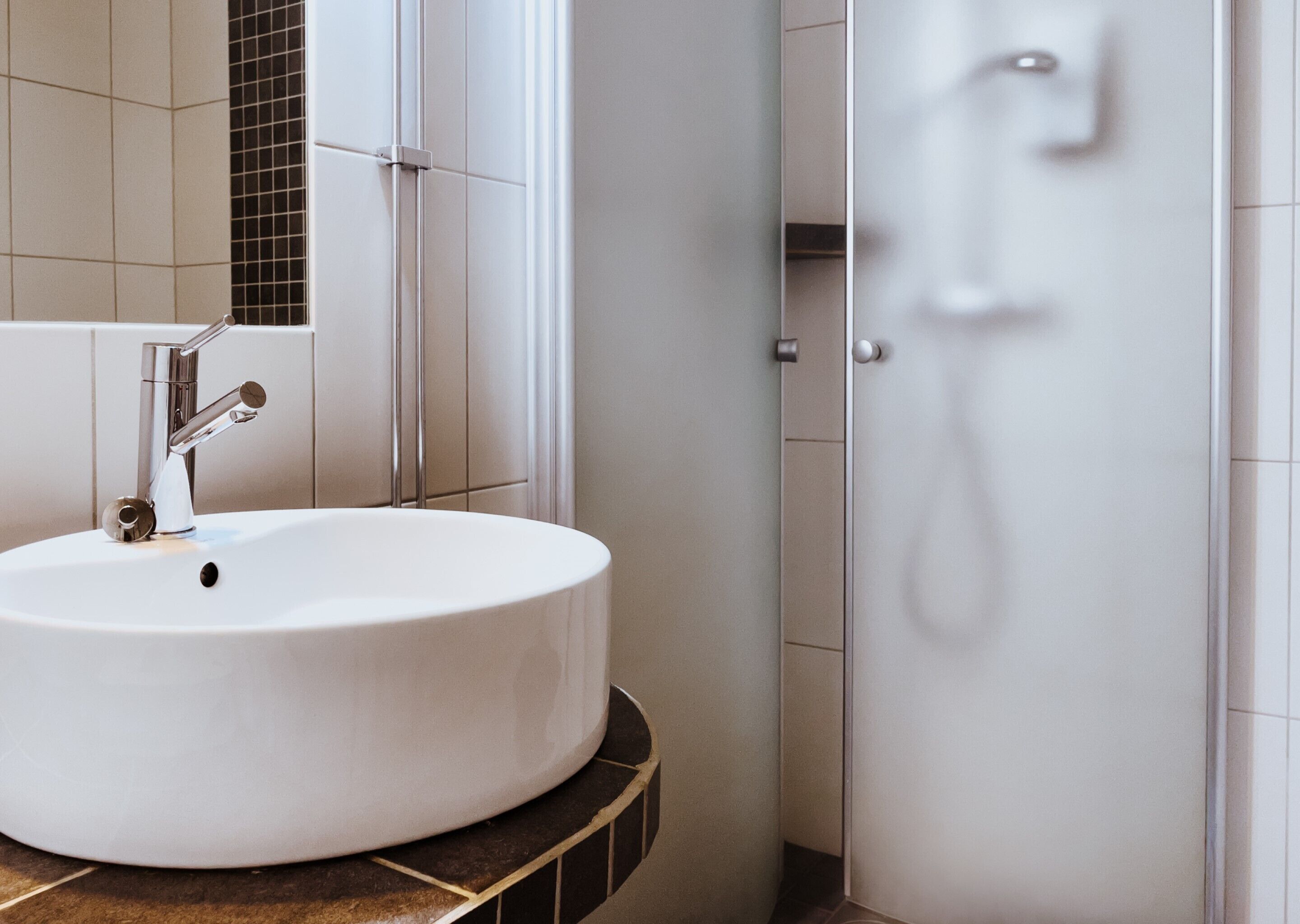 Un baño con lavamanos blanco, un espejo y una puerta de ducha.