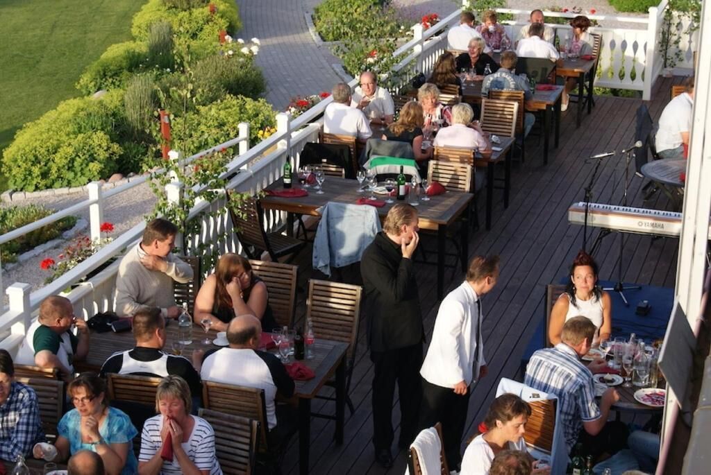 Un espace extérieur aménagé pour les repas, avec plusieurs tables et chaises, entouré d’une clôture blanche et de verdure.