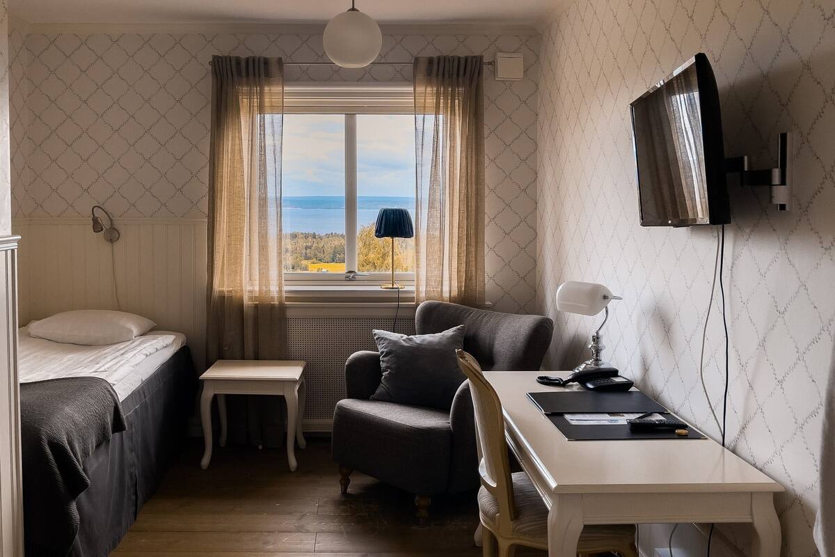 A small, cozy room with a bed, a desk, and a chair. There is a window with a view of the outdoors.