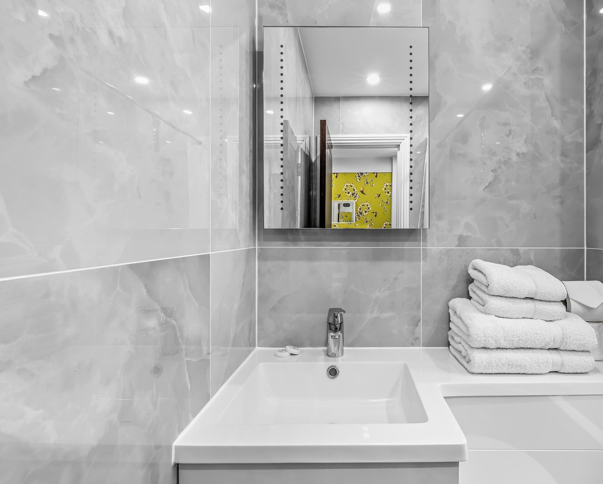 Une salle de bain moderne avec un grand miroir, un lavabo et une pile de serviettes blanches.