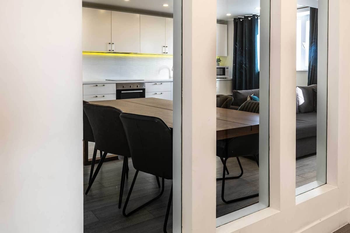 Une cuisine moderne avec des meubles blancs, un plan de travail en bois et un coin repas comprenant une table et des chaises.