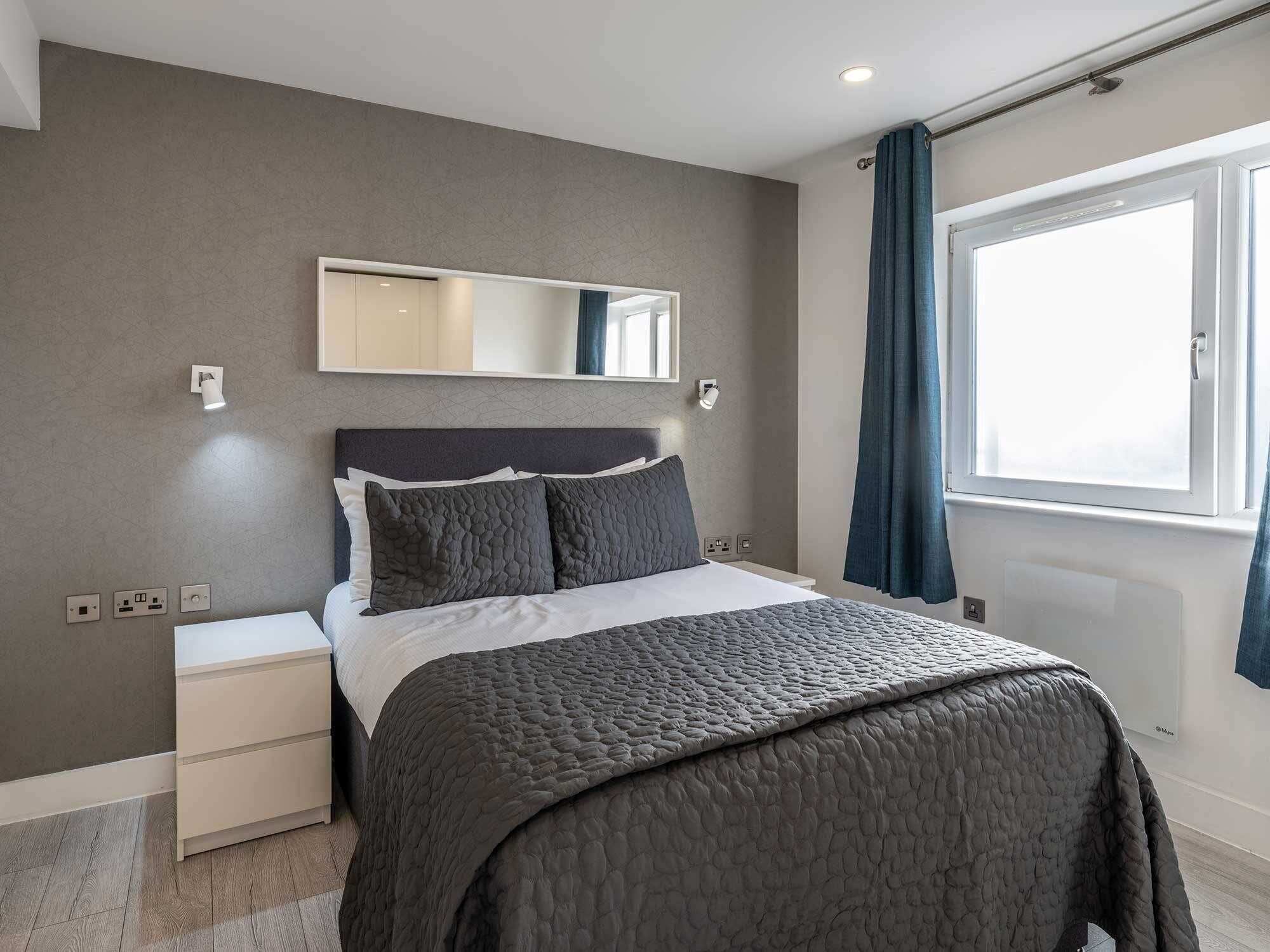 Une chambre moderne avec un lit, des tables de chevet, un miroir et une fenêtre avec des rideaux.
