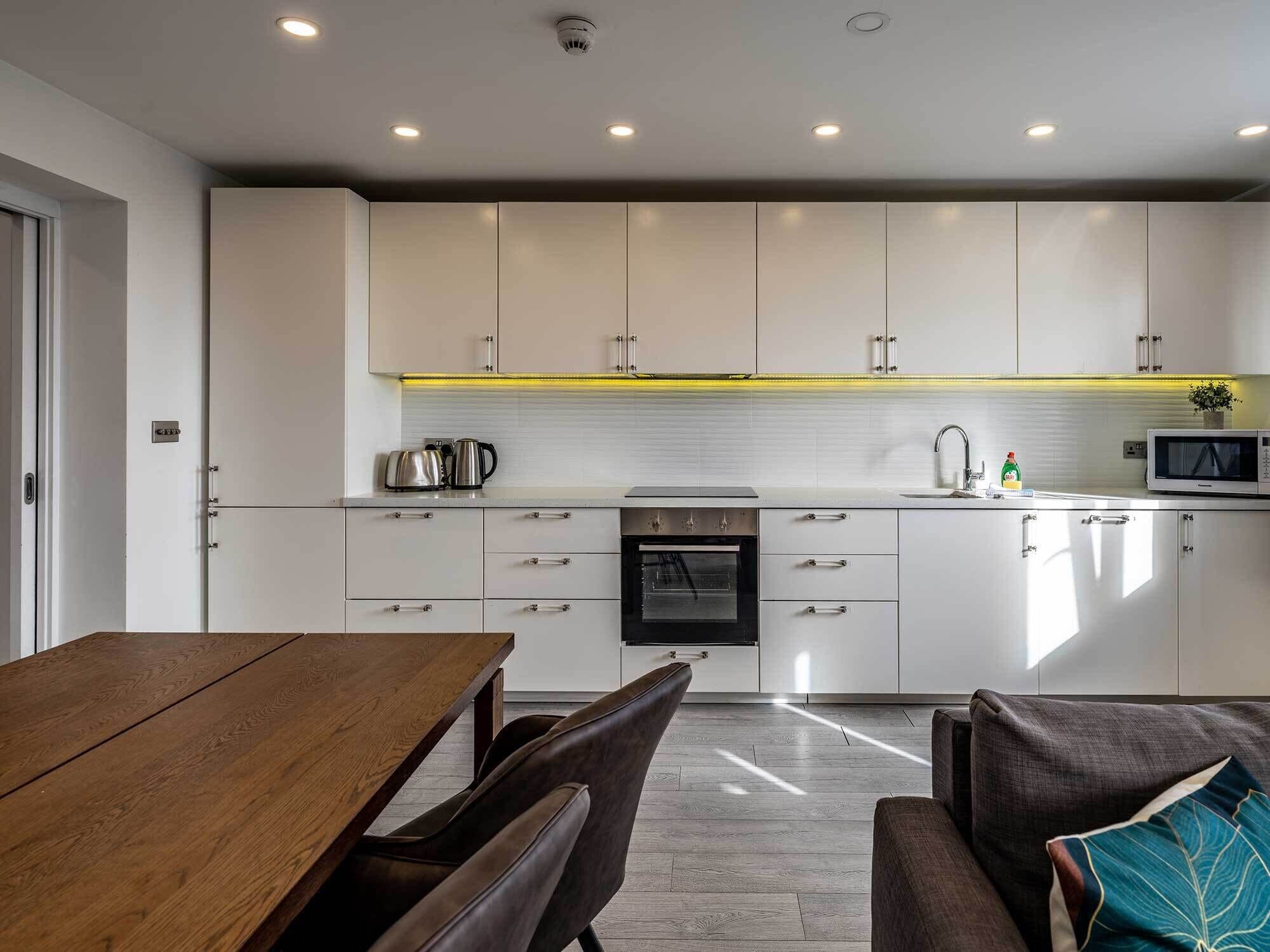 Una cocina moderna con armarios blancos, una mesa de comedor de madera y un horno empotrado.