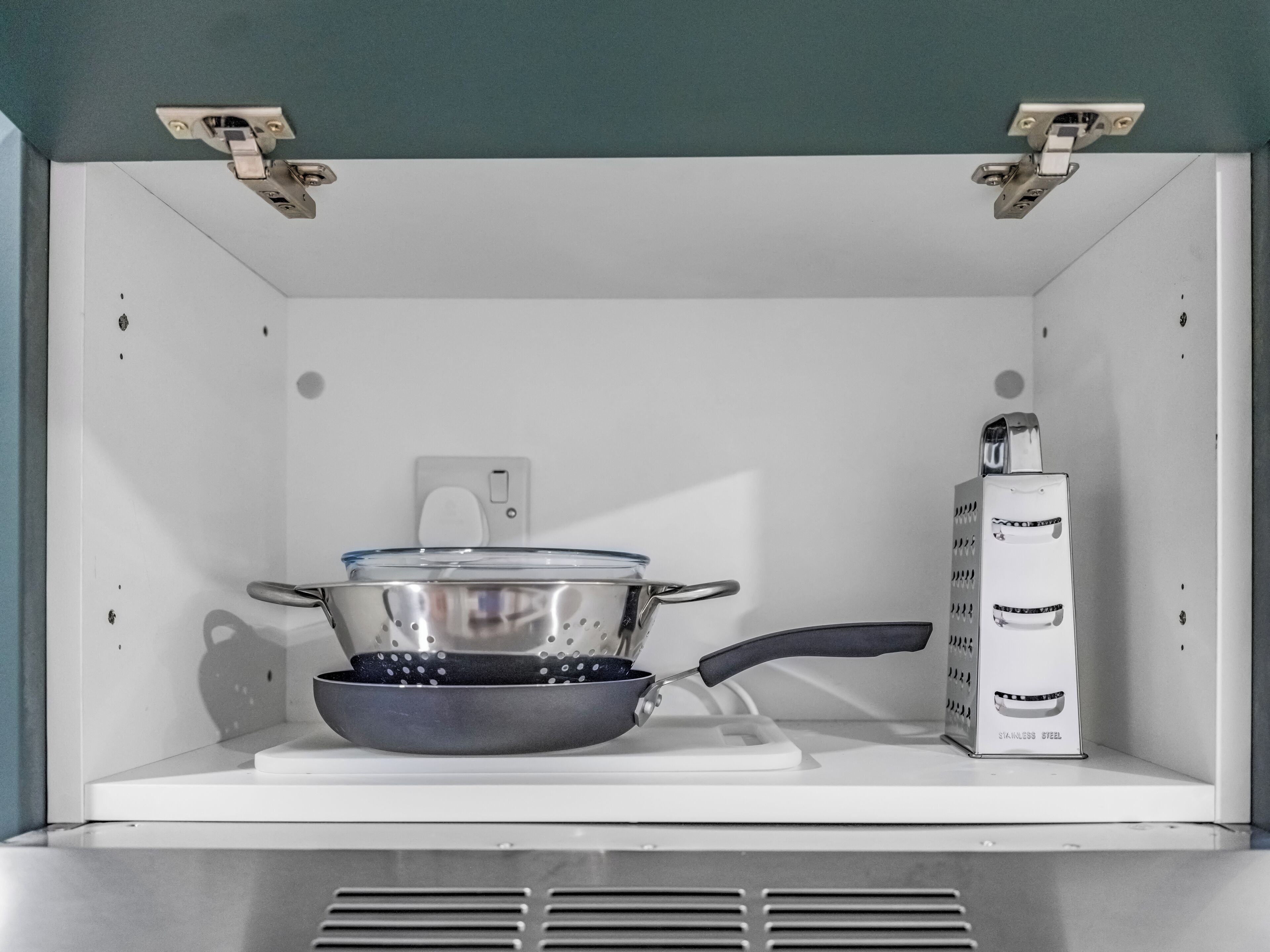 A kitchen with a stove, a frying pan, and a stainless steel grater.