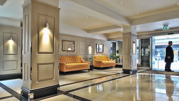 A spacious lobby with a polished floor, two sofas, and a man standing near the entrance. - Chelsea Cloisters Serviced Apartments (London)