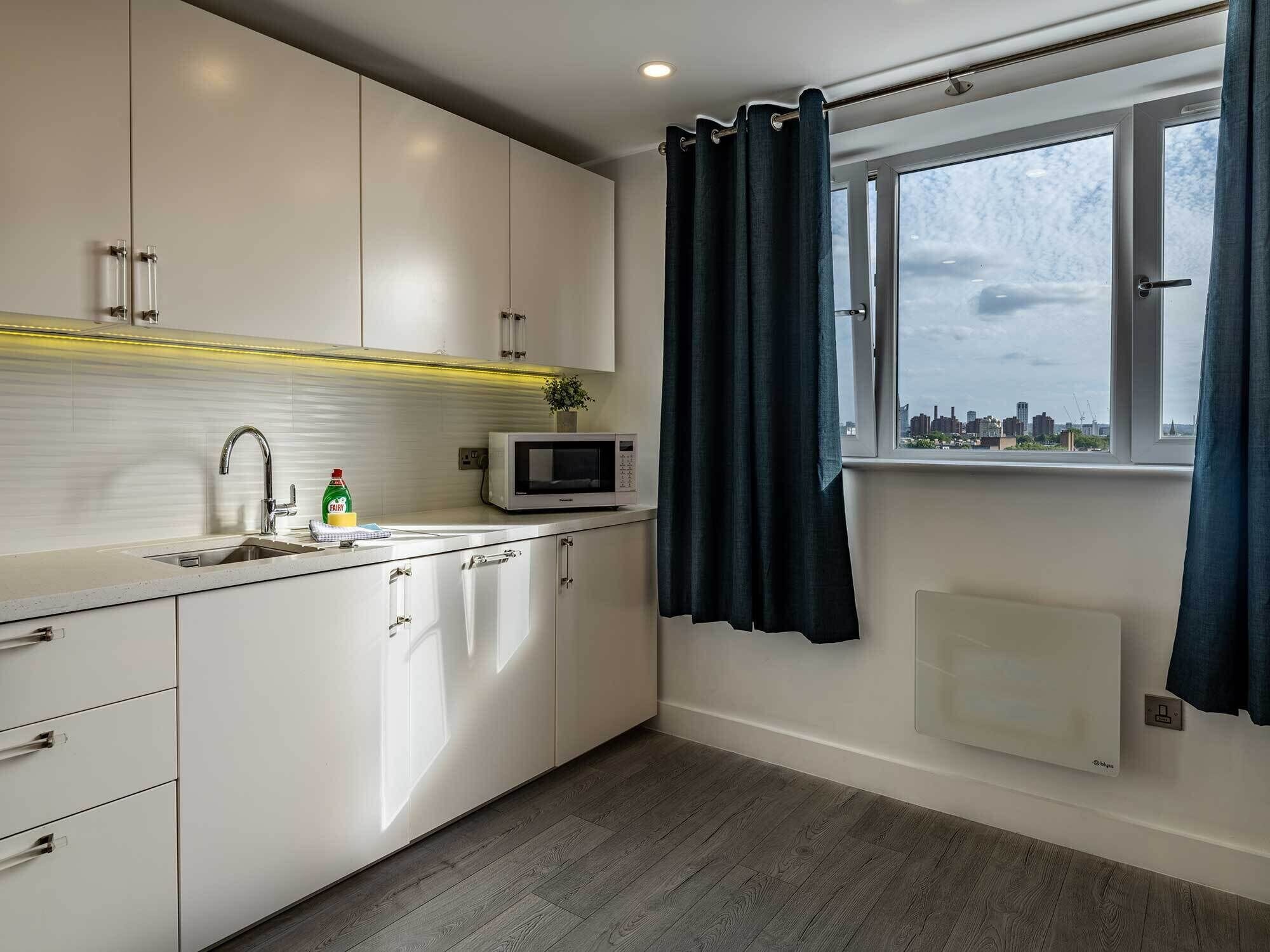 A modern kitchen with white cabinets, a microwave, and a window with curtains.