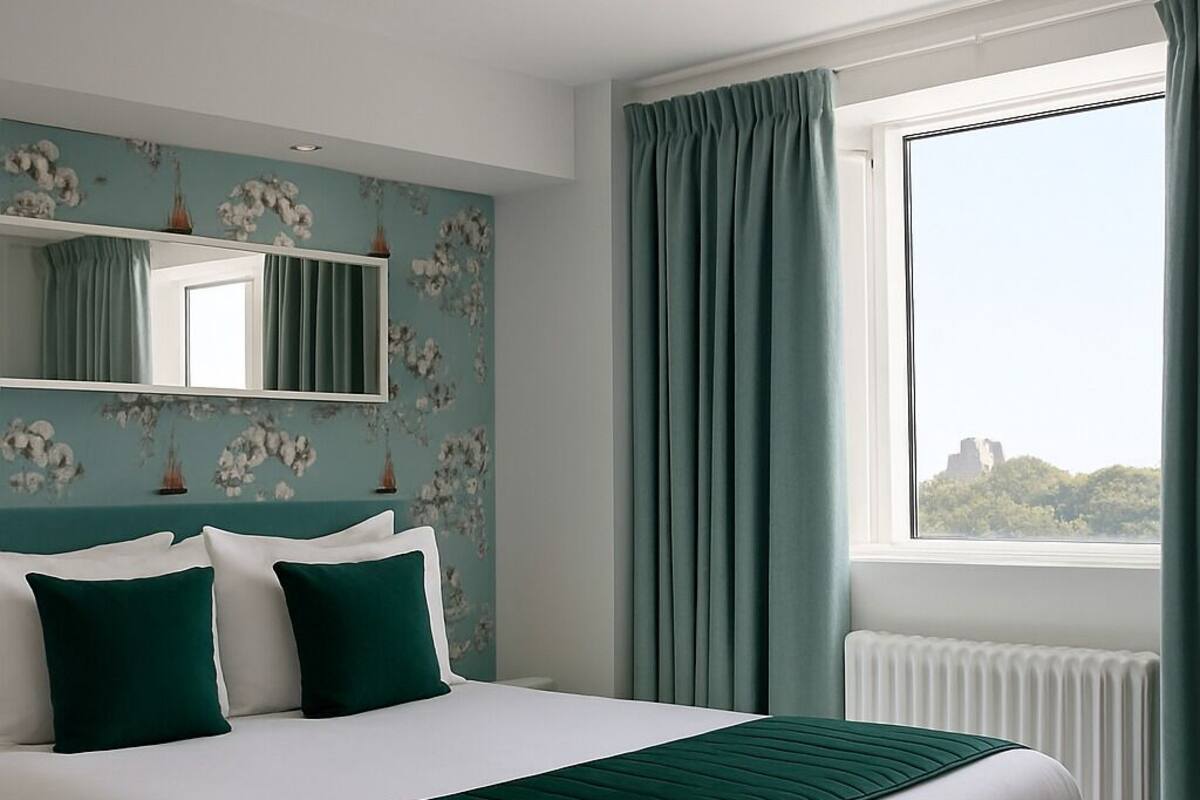Une chambre à coucher moderne avec un grand lit, une fenêtre avec des rideaux, un radiateur et un papier peint à motifs floraux.