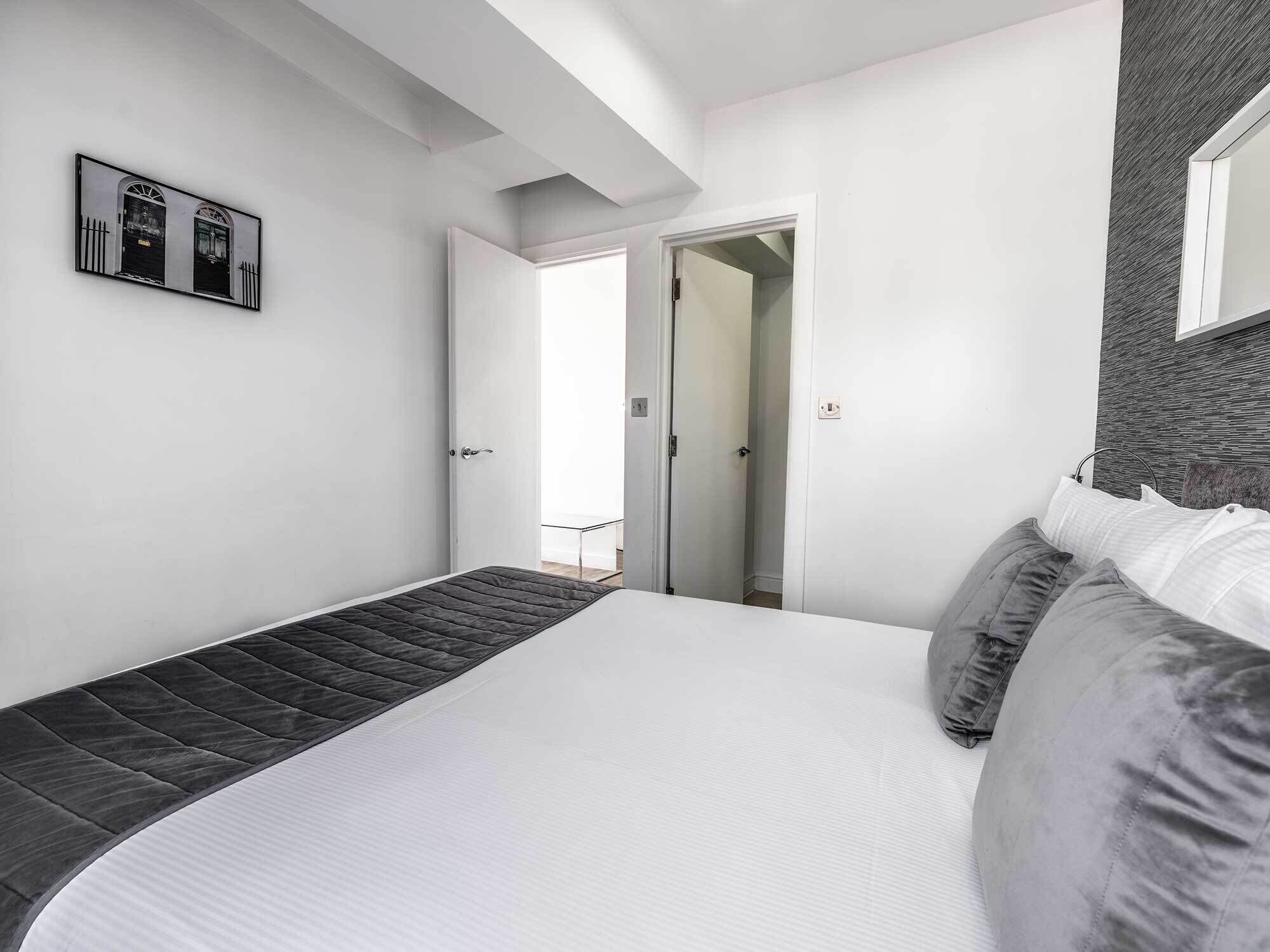 Une chambre moderne avec un grand lit, un petit canapé et une porte donnant sur un couloir.