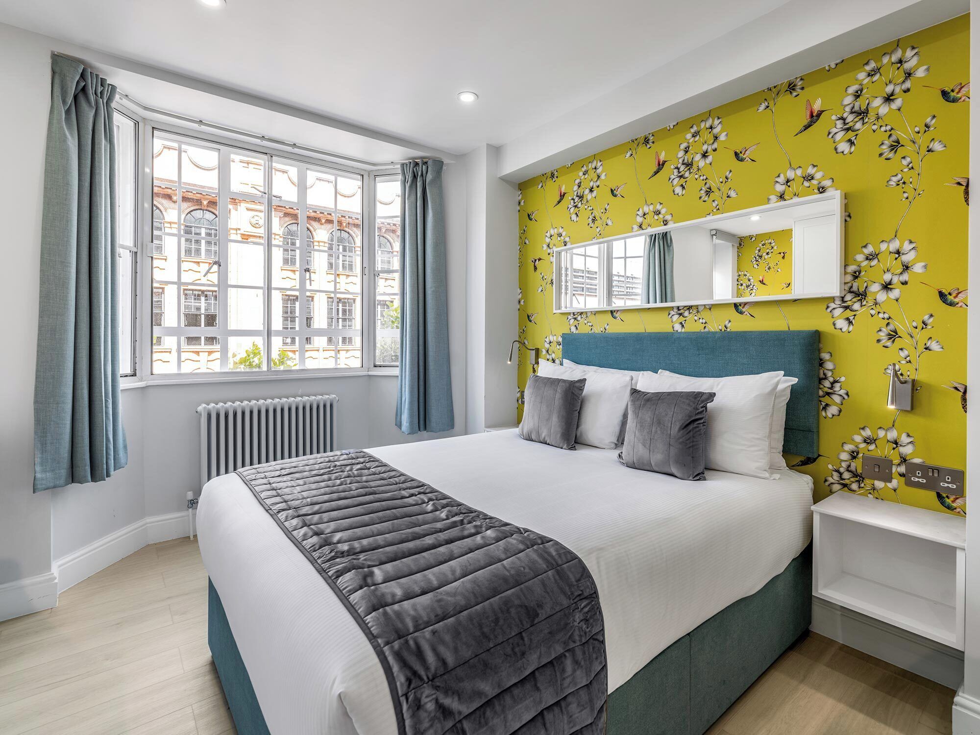 Una camera da letto moderna con un letto grande, una finestra con tende, un termosifone e una parete con carta da parati a motivi floreali.