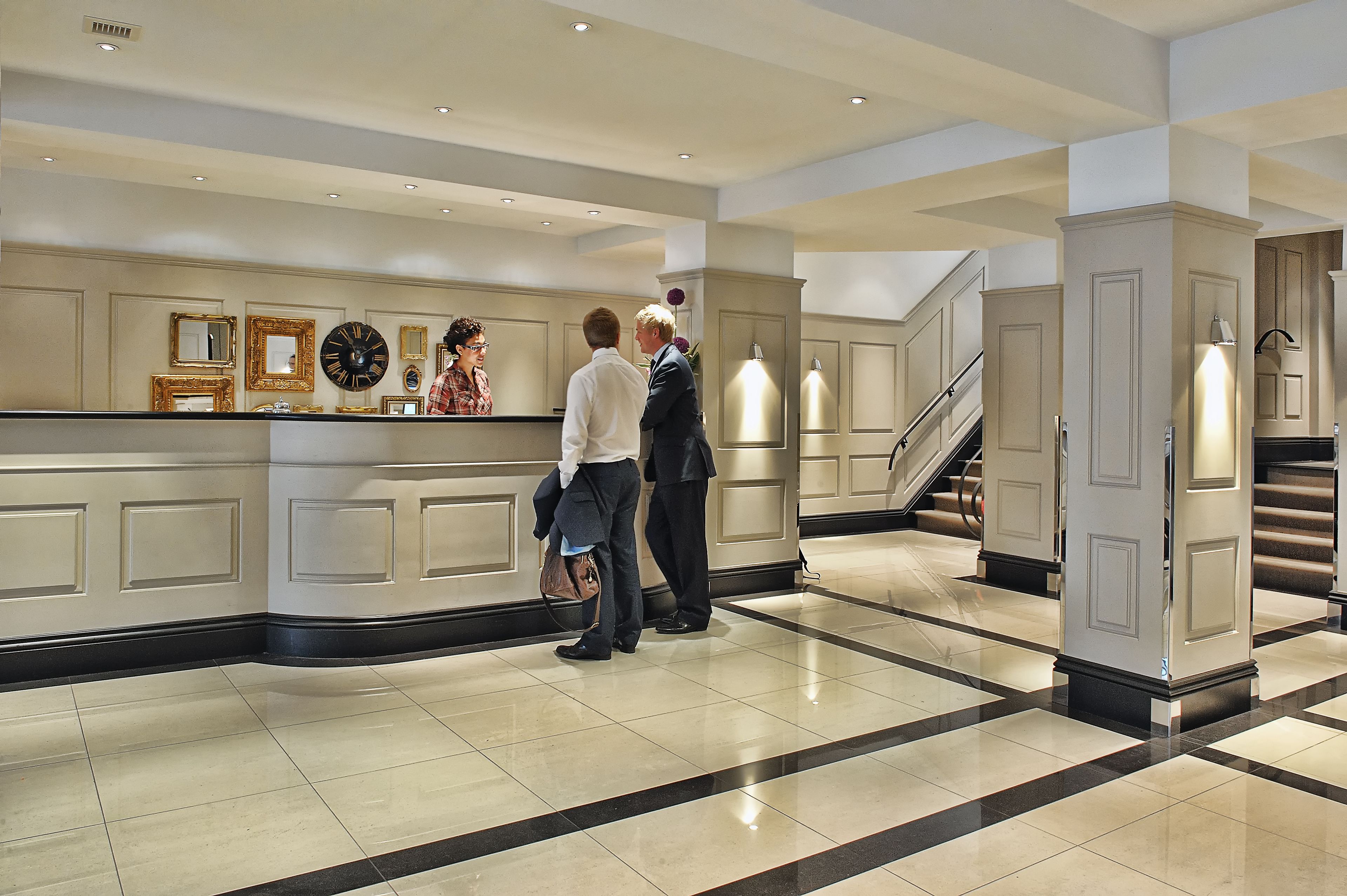 A hotel reception area with a counter, framed mirrors, and a staircase.