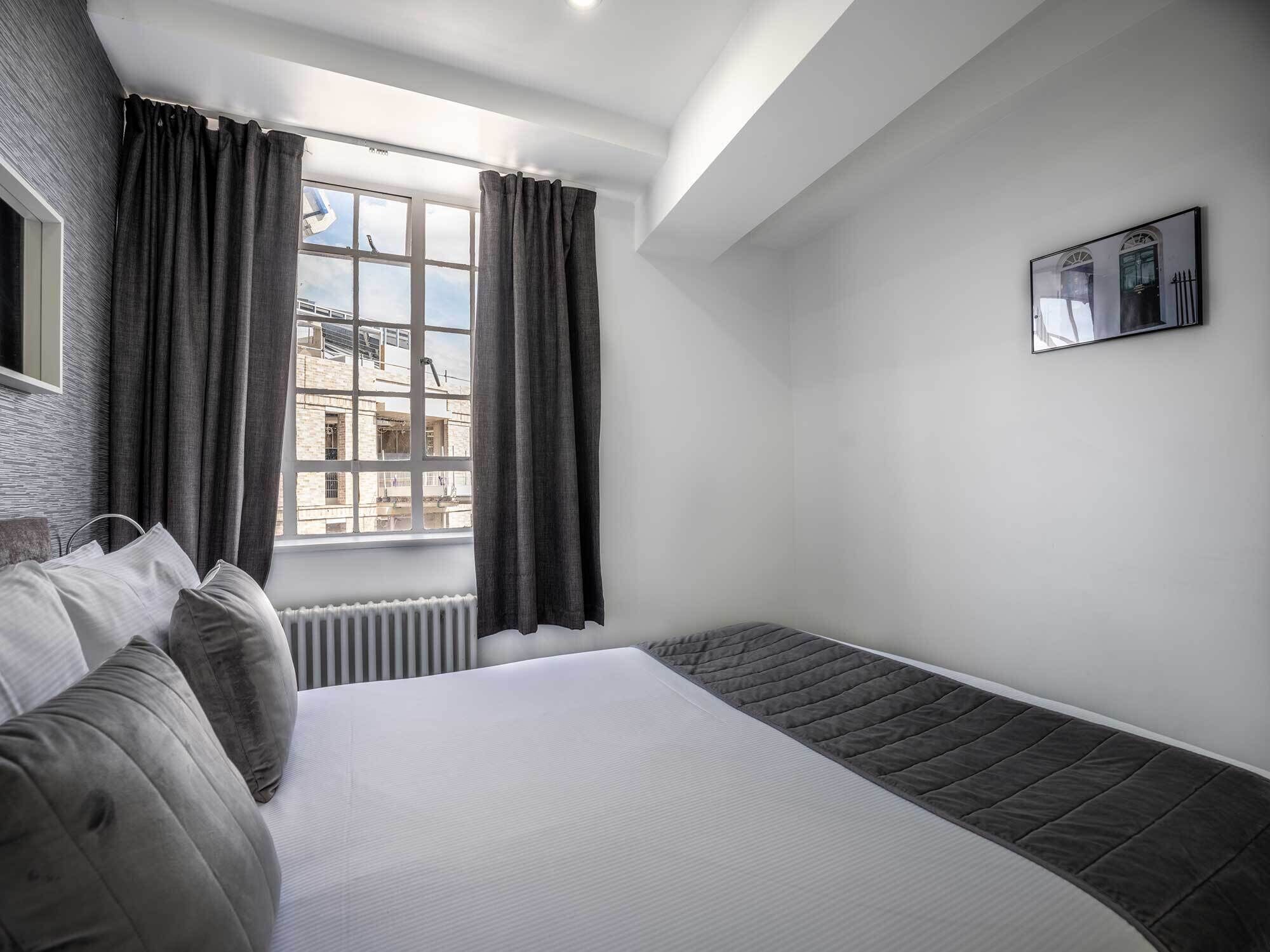 Una habitación de hotel moderna con una cama grande, vistas a edificios y un cuadro en la pared.