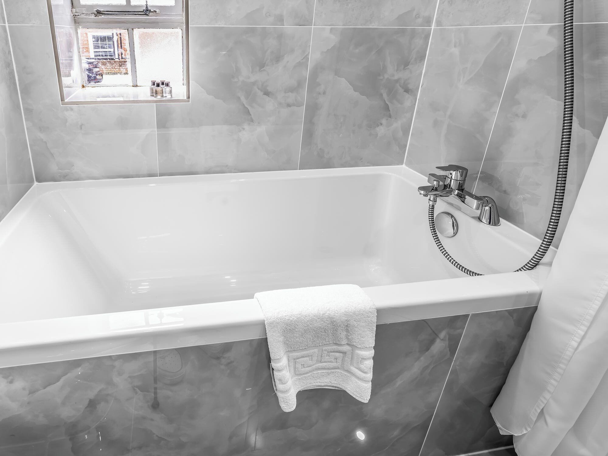 A modern bathroom with a rectangular bathtub, a handheld showerhead, and a towel hanging on the side.