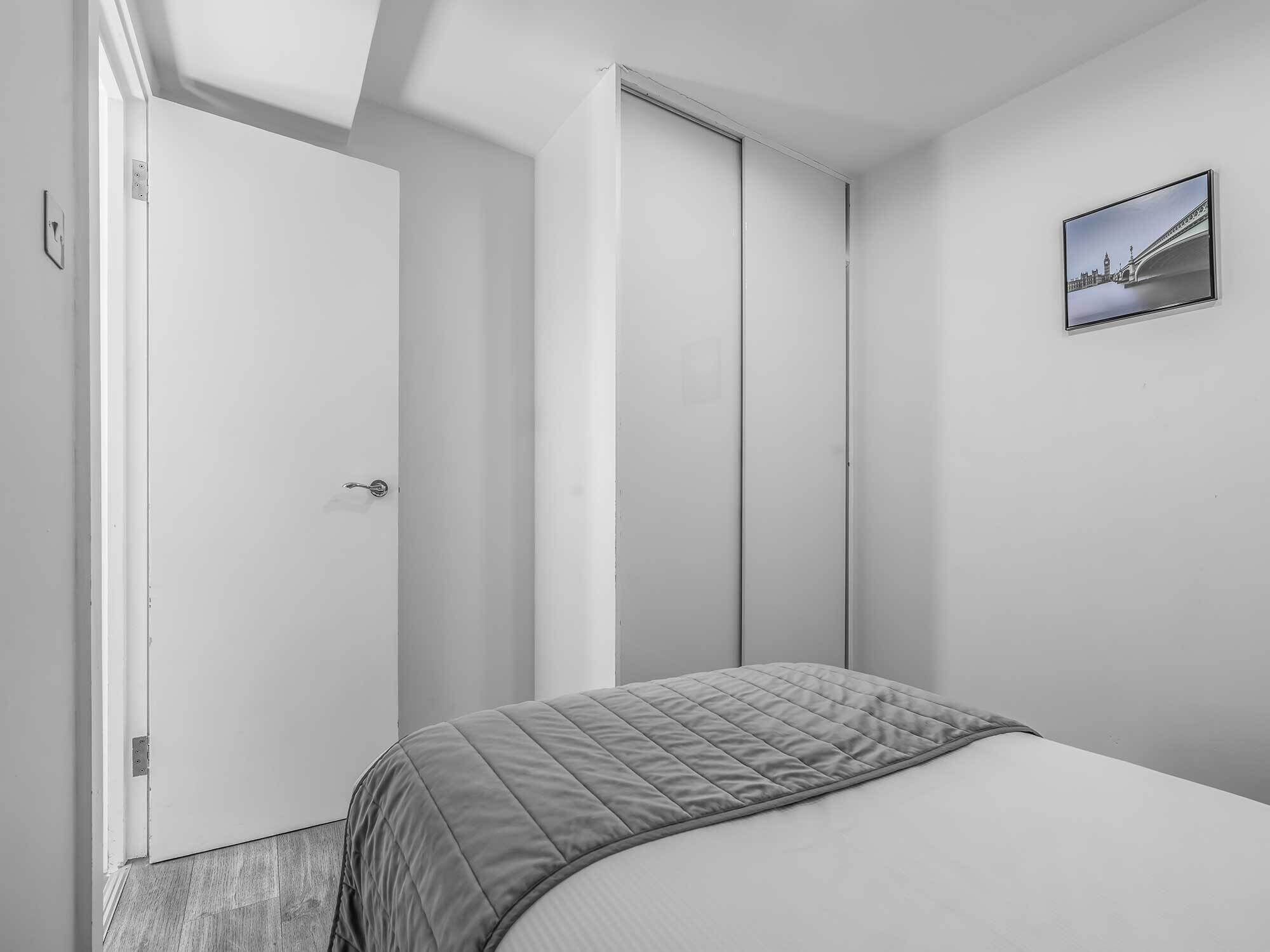 A minimalist bedroom with a bed, a door, and a framed picture on the wall.