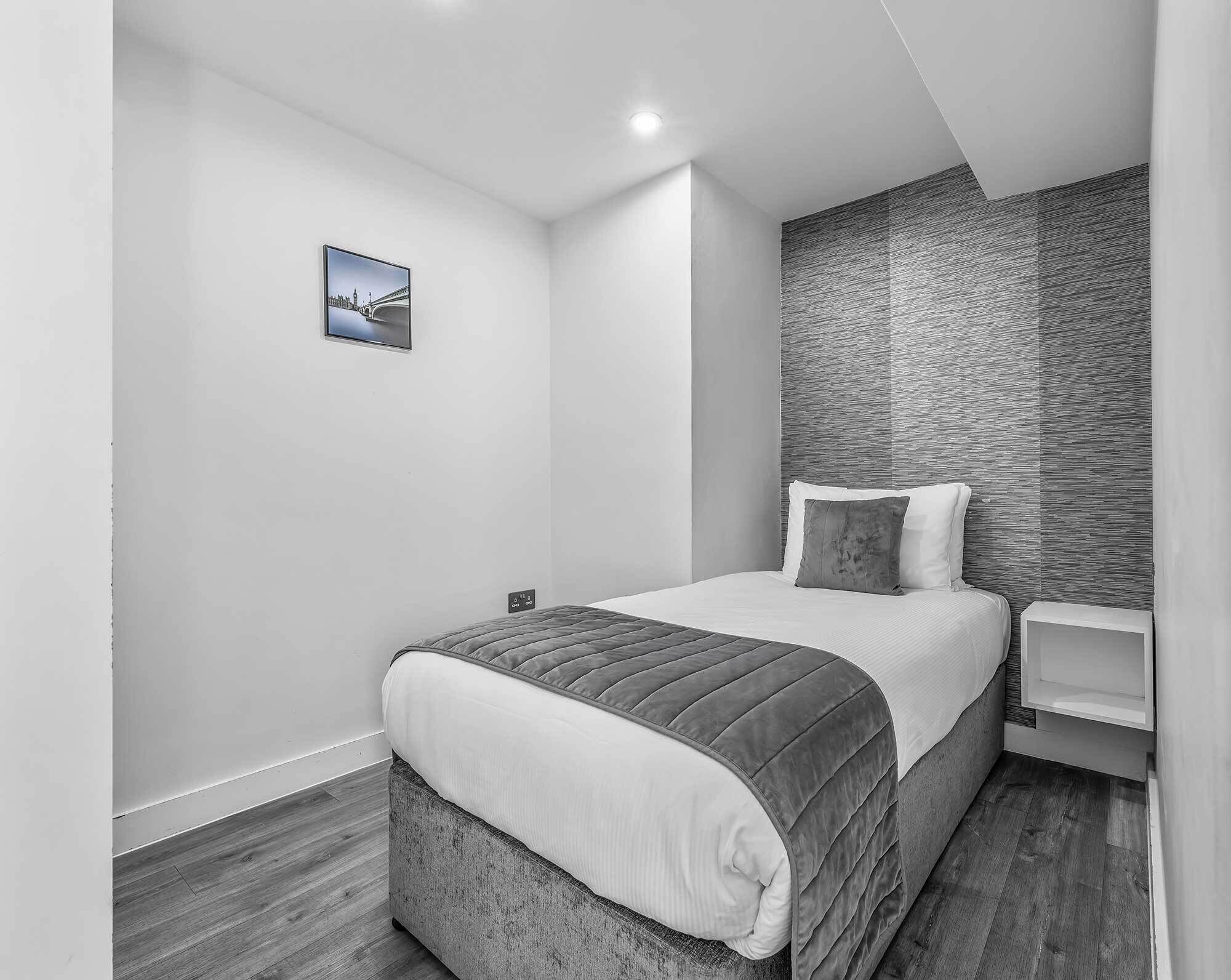 A modern bedroom with a bed, a nightstand, a wall-mounted TV, and a textured wall.