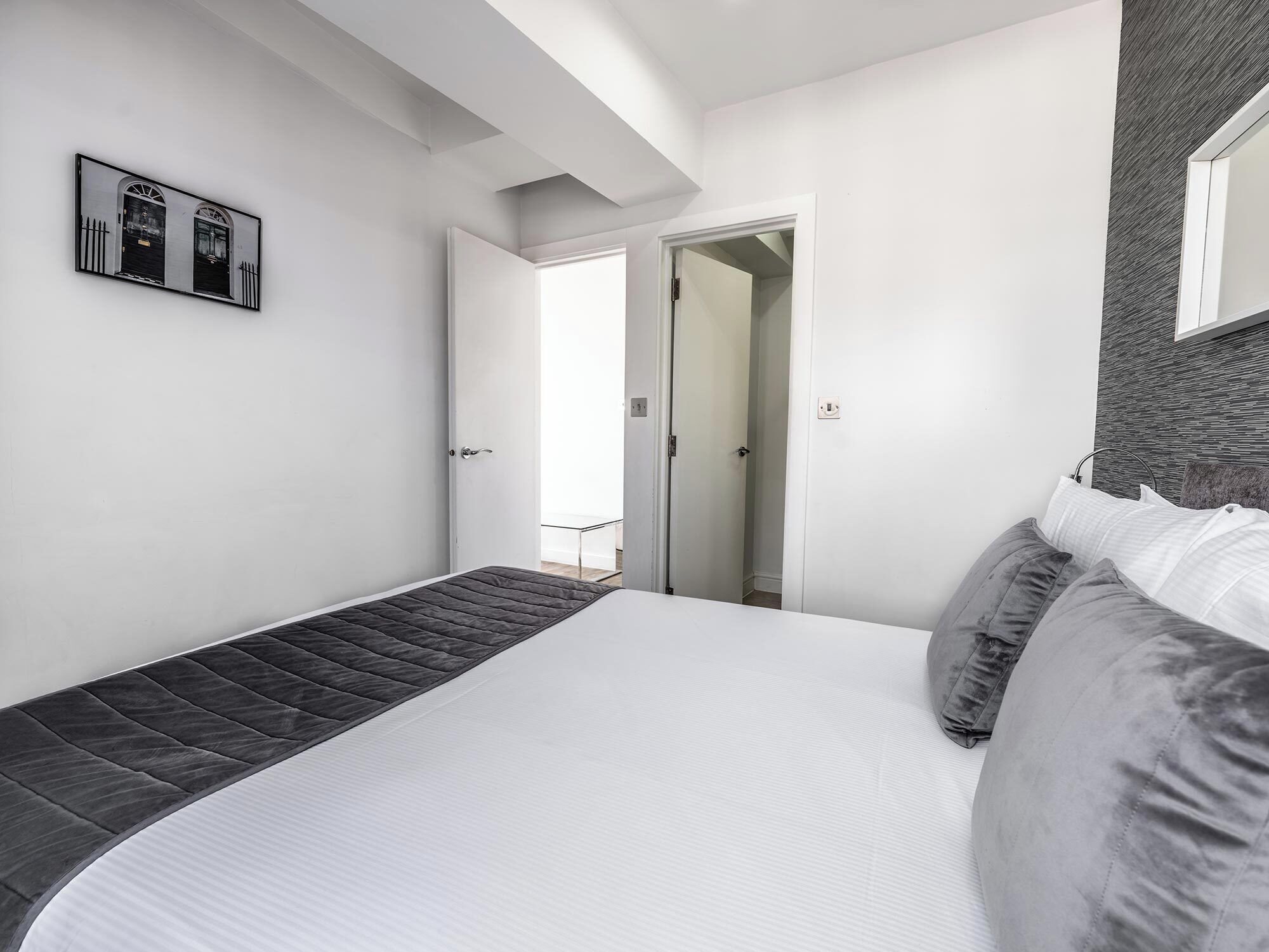 Une chambre moderne avec un lit, une table de chevet et une porte donnant sur une autre pièce.