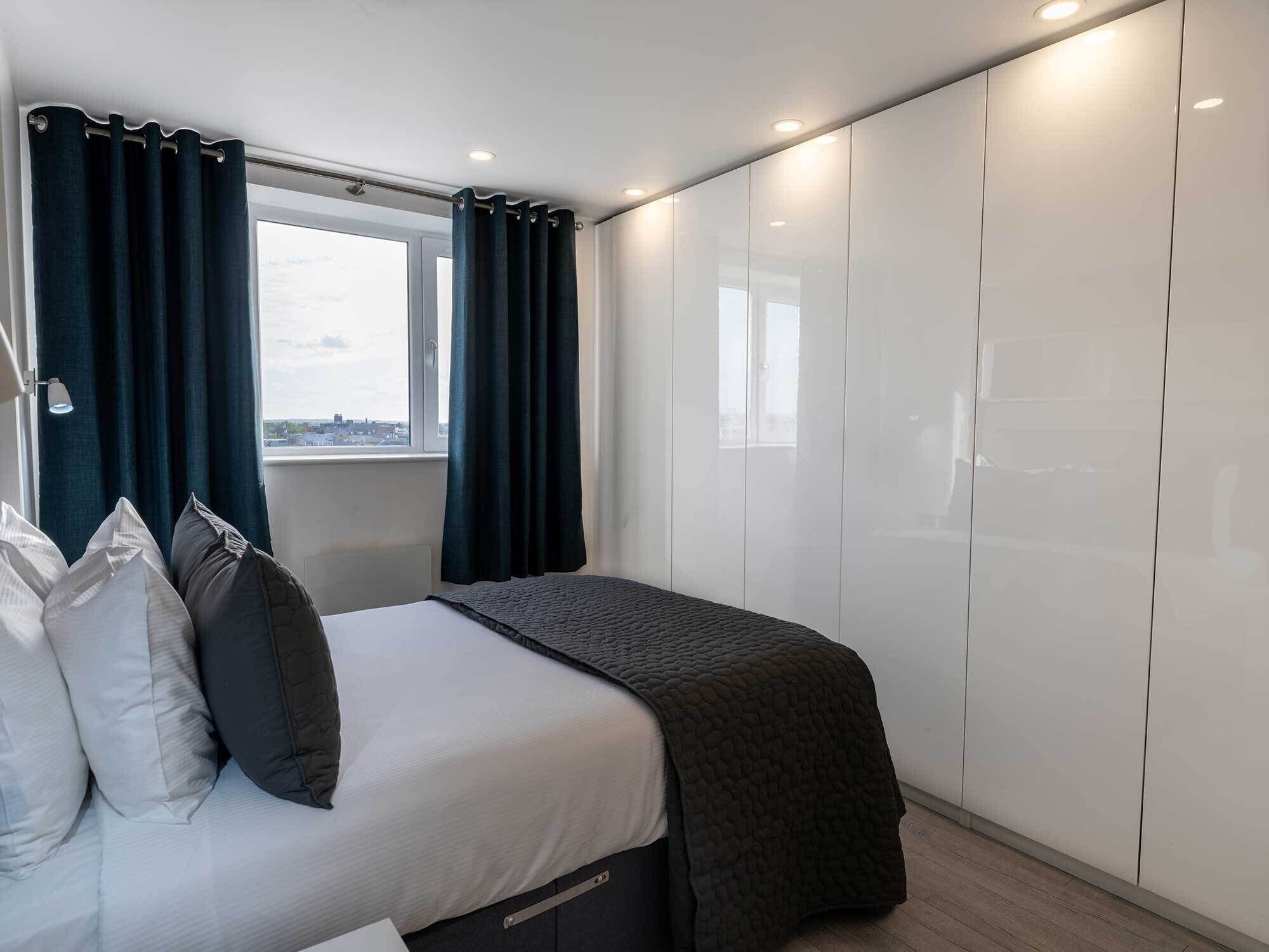Un dormitorio con cama, cortinas oscuras, una ventana y un armario.