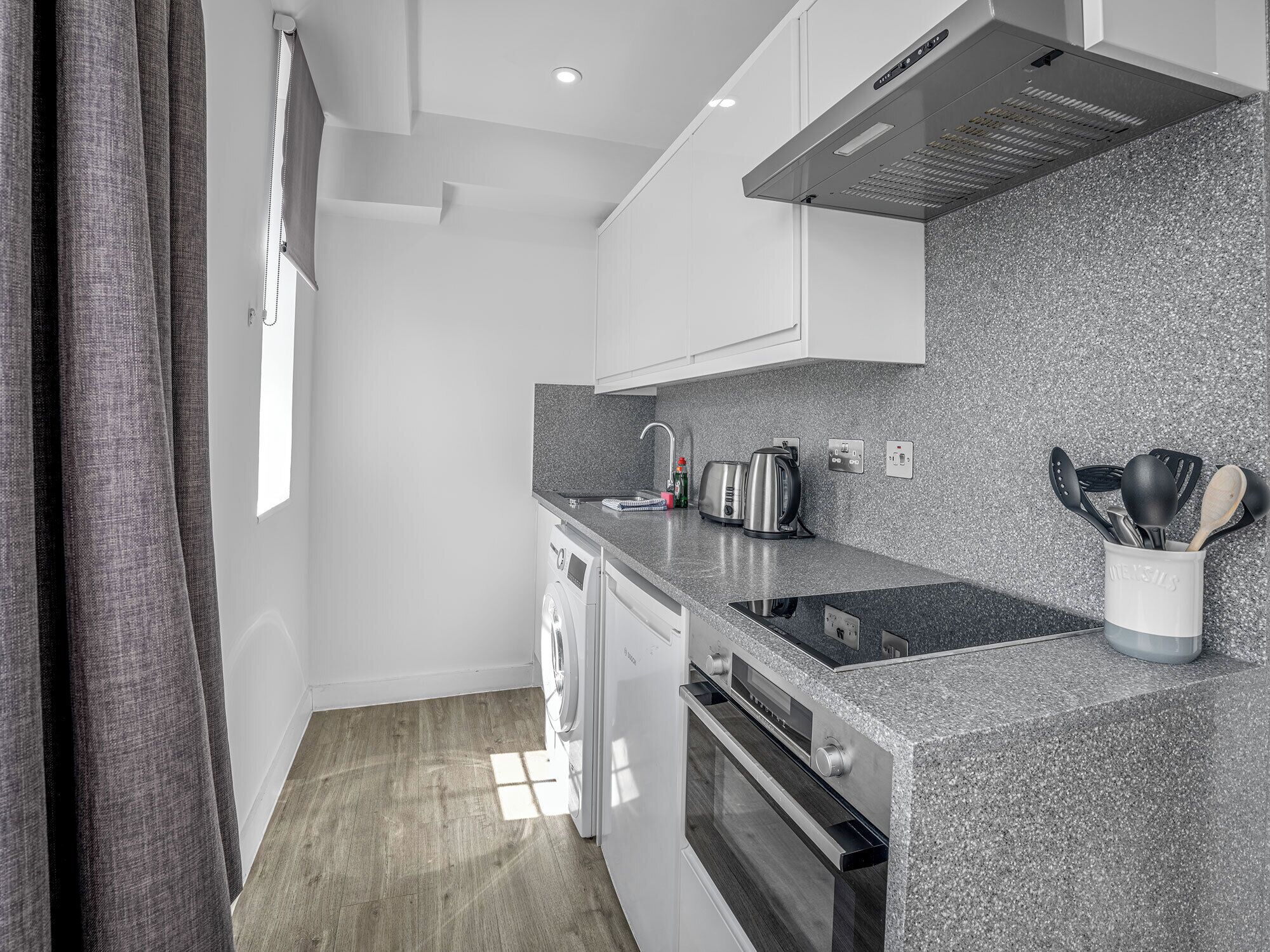 Een compacte keuken met een granieten aanrechtblad, roestvrijstalen apparatuur en uitzicht naar buiten door een raam.