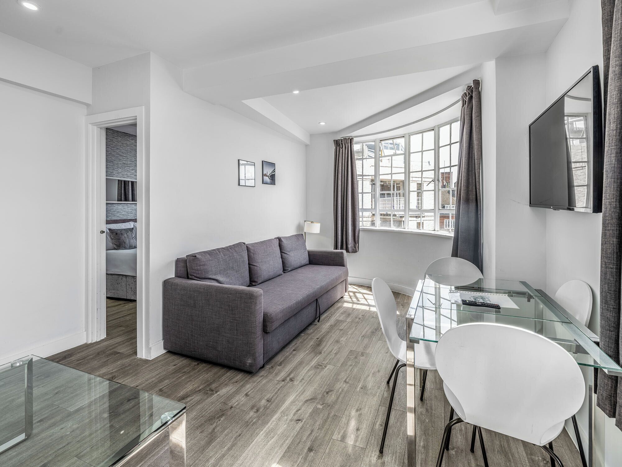 Ein modernes Wohnzimmer mit einem grauen Sofa, einem Glastisch und einem an der Wand befestigten Fernseher.
