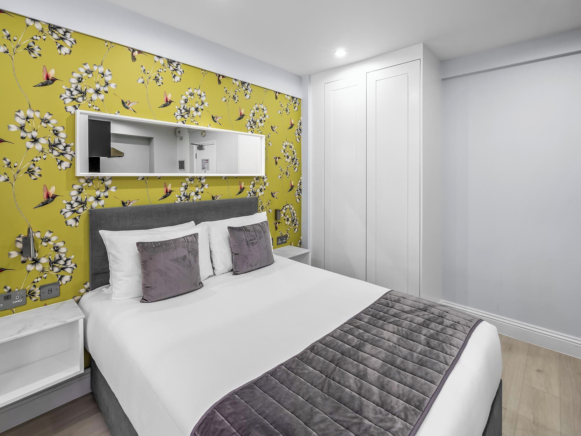 Un dormitorio con cama, mesita de noche, armario y un papel tapiz floral en la pared.