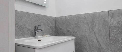 A modern bathroom with a white vanity, a mirror with lights, and grey marble tiles.