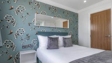A bedroom with a bed, a nightstand, a mirror, and a wooden door.