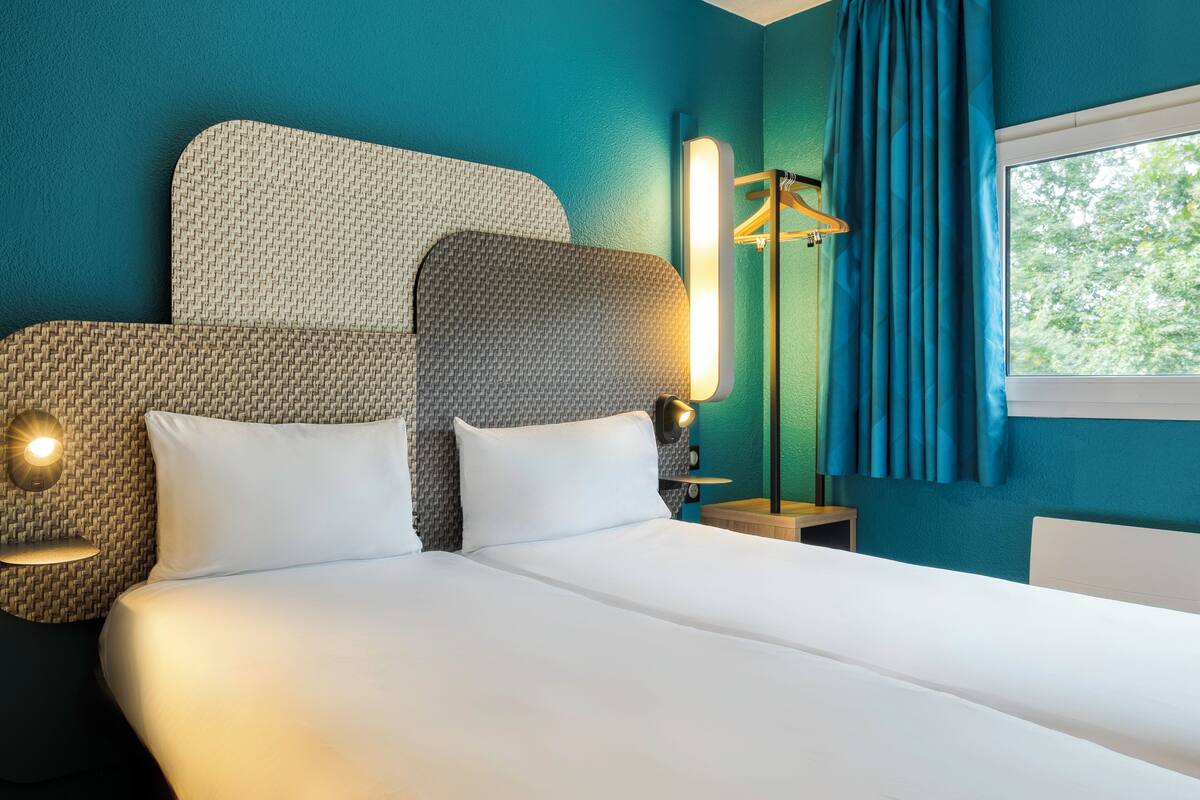 Une chambre d’hôtel avec un grand lit, deux tables de chevet avec des lampes, une lampe sur pied et une fenêtre avec des rideaux.