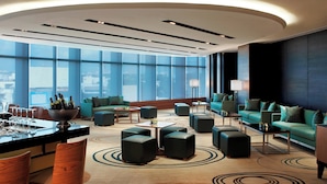 Un hall d’hôtel moderne doté d’un plafond incurvé, de grandes fenêtres et d’un ensemble d’espaces de détente comprenant des canapés et des poufs.