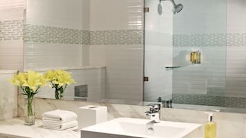 A modern bathroom with a large mirror, white marble countertop, and a glass shower enclosure.