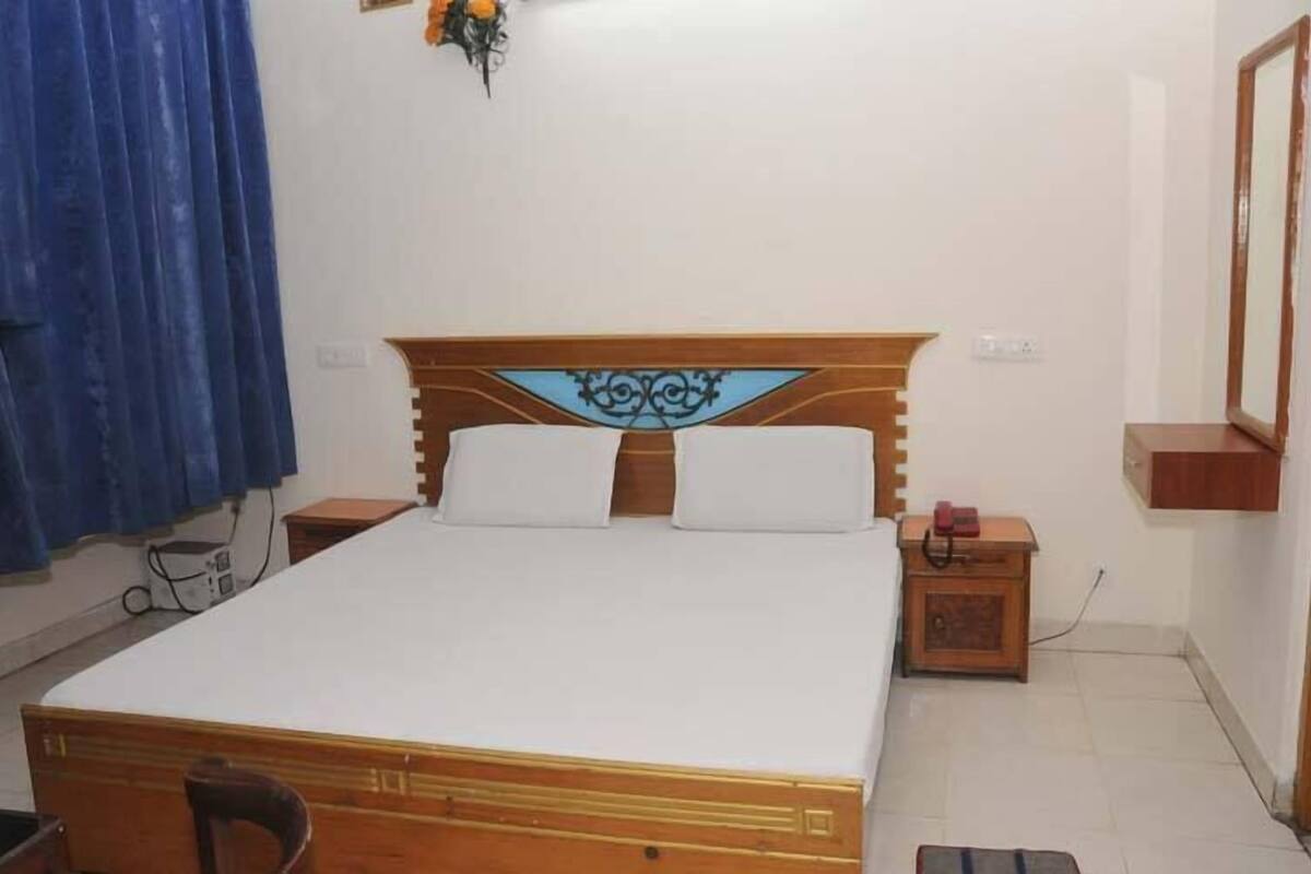 Uma cama de solteiro com cabeceira de madeira e roupa de cama branca em um quarto com piso de azulejos.