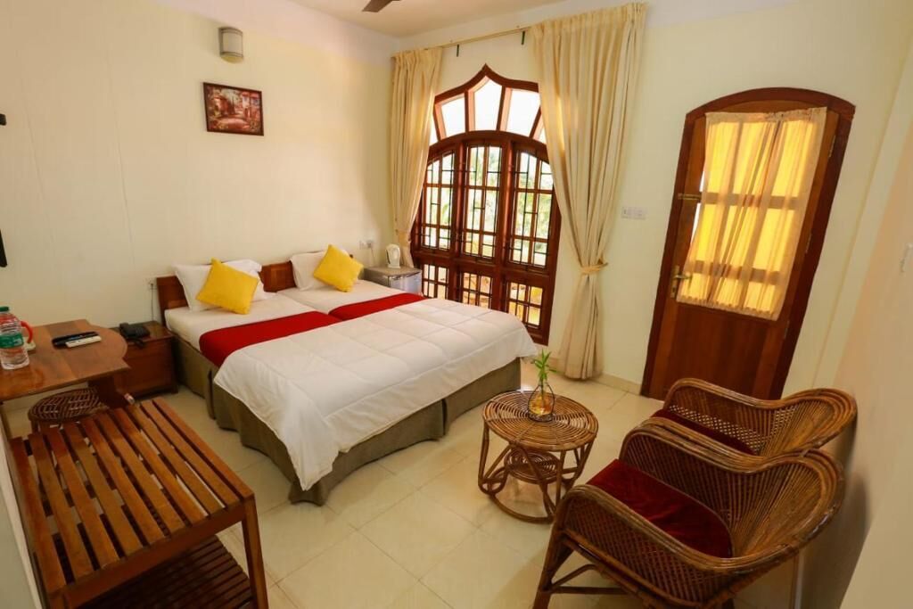 A bedroom with a bed, a bedside table, a chair, a small round table, and a window with curtains.