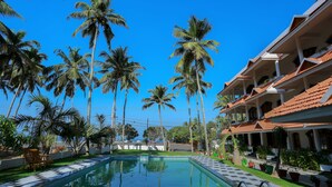 A swimming pool surrounded by palm trees and a building with a tiled roof. - Sanctum Spring (Varkala)