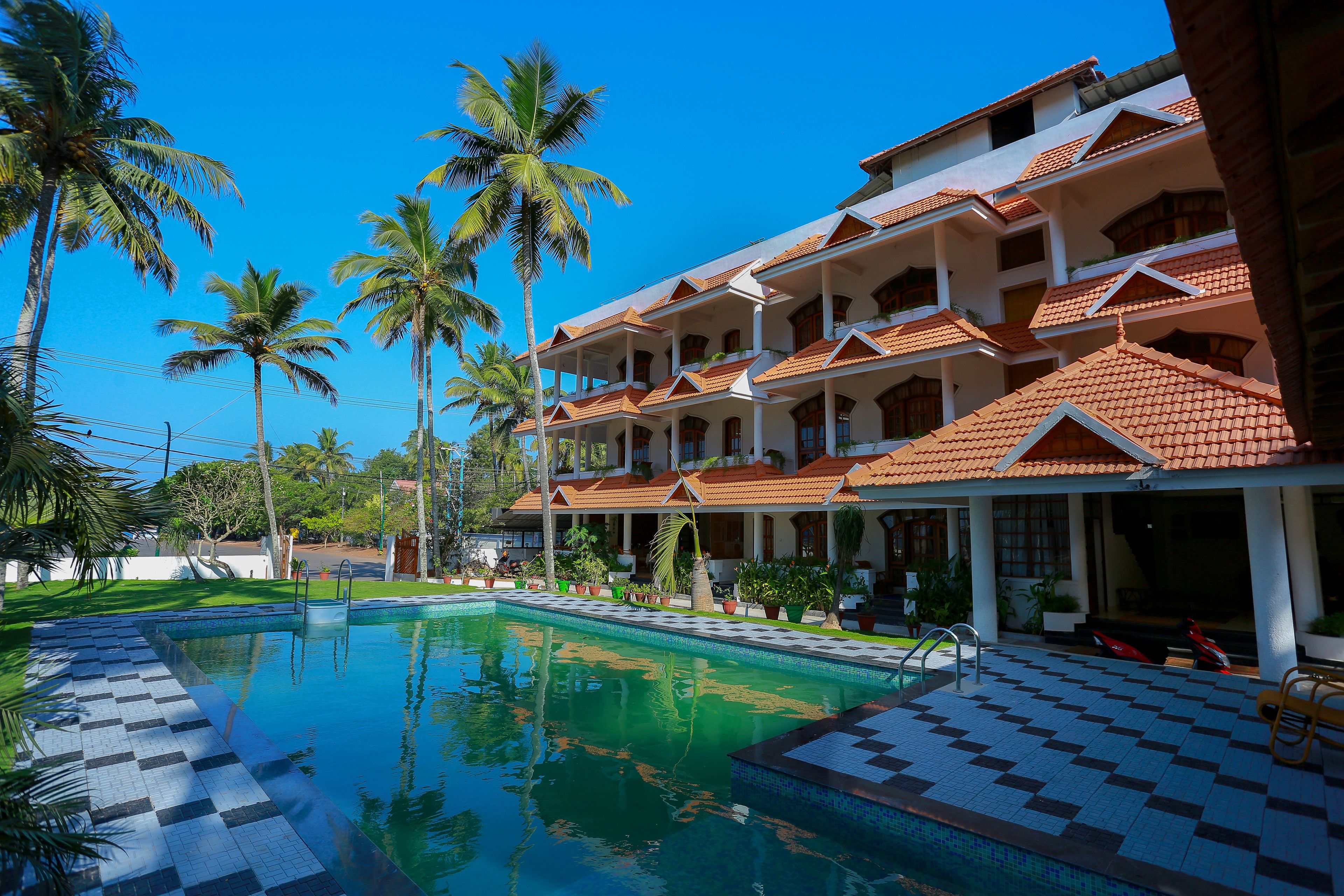 A hotel with a swimming pool, palm trees, and a tiled deck.
