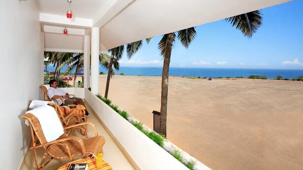 A balcony with wicker chairs, a view of the beach, and a palm tree. - Sanctum Spring (Varkala)