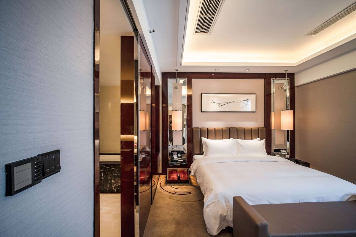 A modern hotel room with a large bed, bedside tables, a desk, and a chair.
