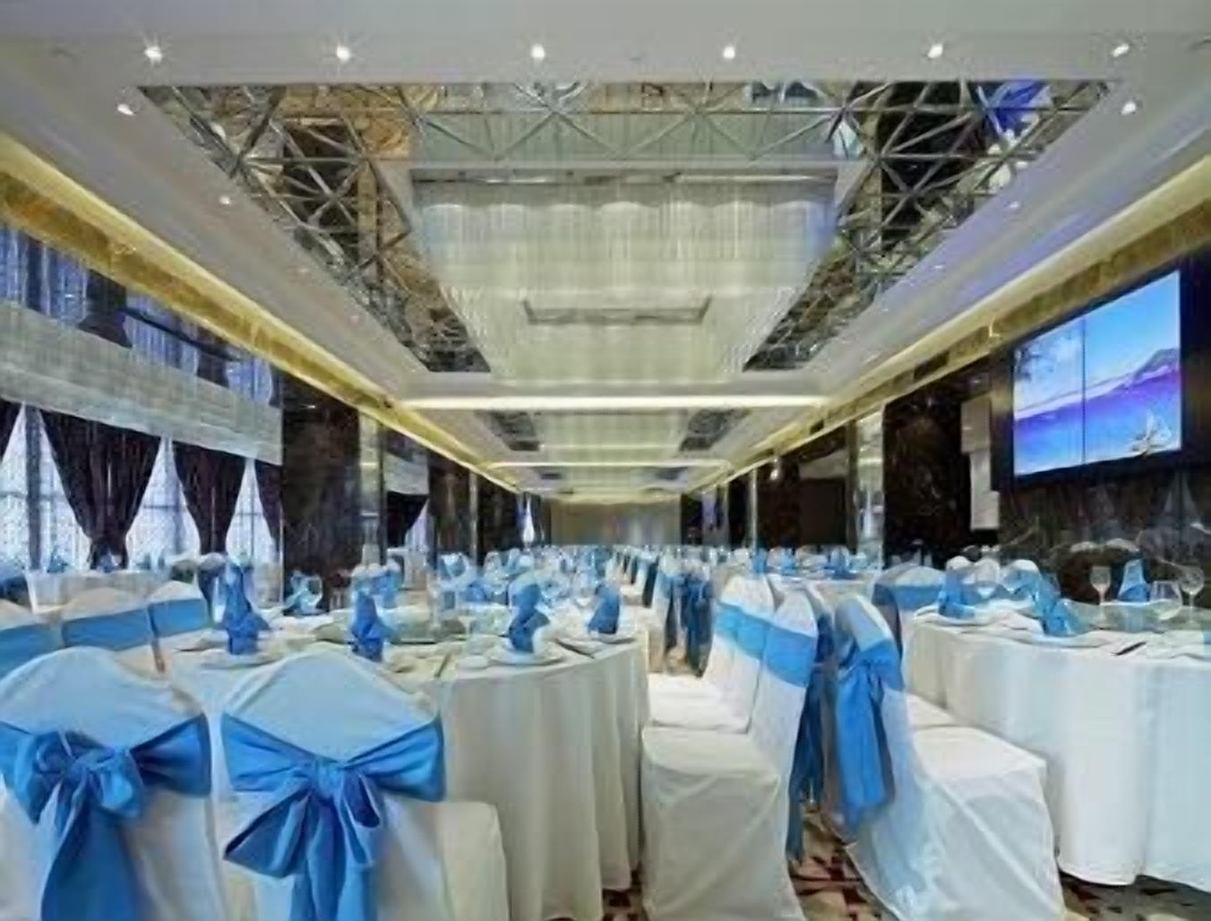 A banquet hall with rows of round tables, each covered with white tablecloths and blue sashes.