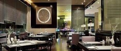 Interior de un restaurante moderno con suelo de madera, mesas y sillas de tonos oscuros, y una obra de arte central en la pared.