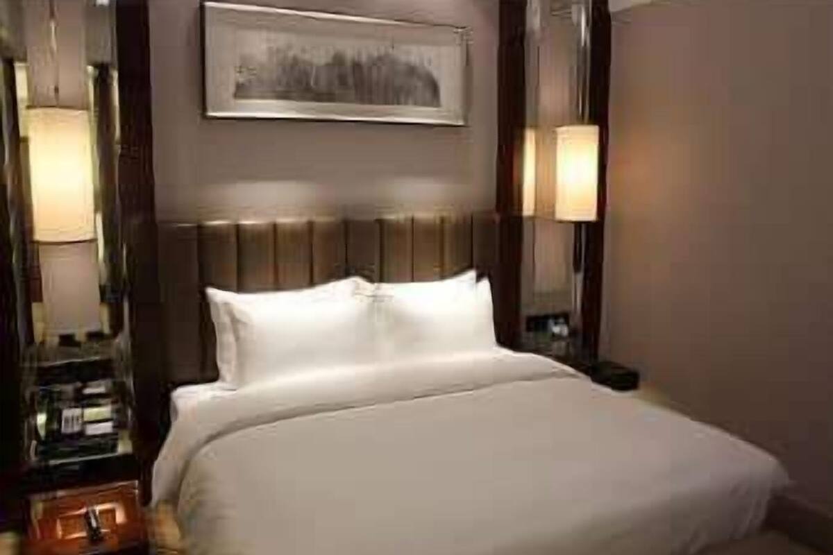 A hotel room with a large bed, a nightstand, a lamp, and a framed picture on the wall.