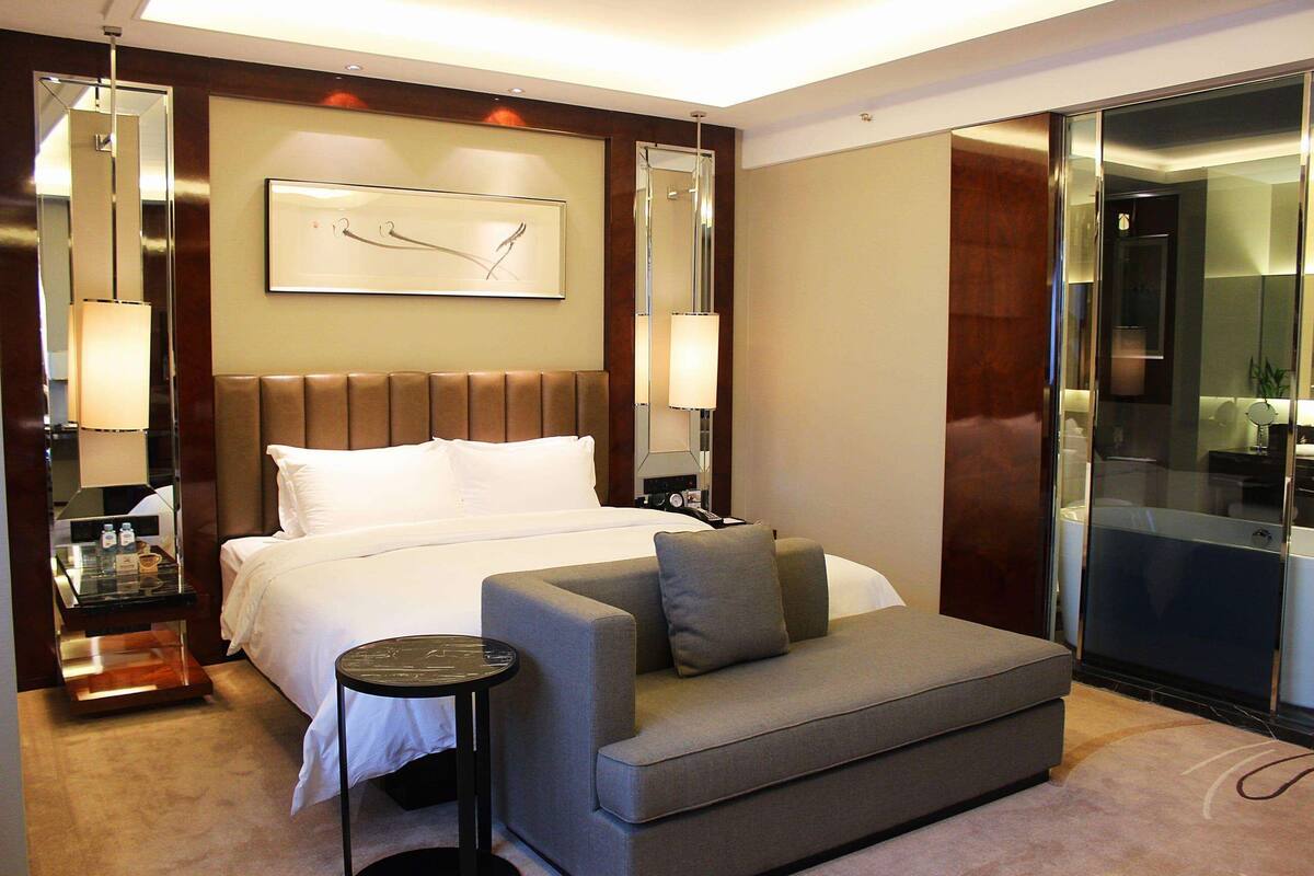 A hotel room with a bed, a sofa, a small table, and a mirror.