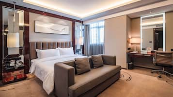 A modern hotel room with a large bed, a sofa, a desk, and a mirror.