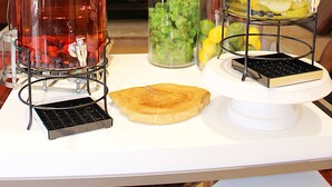 A beverage station with large glass jars containing fruit-infused drinks, a slice of toast, and a small black object on a white table. - Hilton Garden Inn Falls Church (Falls Church)