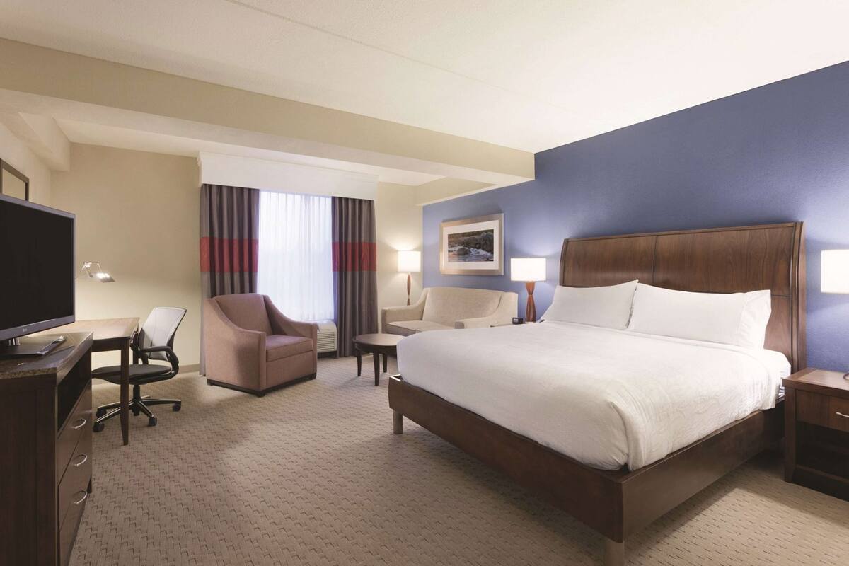 A hotel room with a bed, desk, chair, and a television.