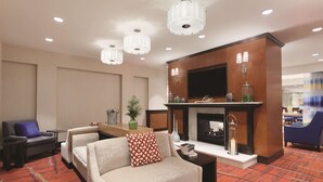 A modern hotel lobby with a fireplace, seating area, and a television mounted on the wall. - Hilton Garden Inn Falls Church (Falls Church)